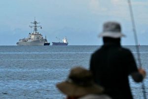 The USS Gravely warship is seen at a distance off the coast of Port of Spain on October 26, 2025, as fishermen look from the Trinidadian capital. The US warship will visit Trinidad and Tobago for joint exercises near the coast of Venezuela amid Washington's campaign against alleged drug traffickers in the region. (Photo by Martin BERNETTI / AFP)
